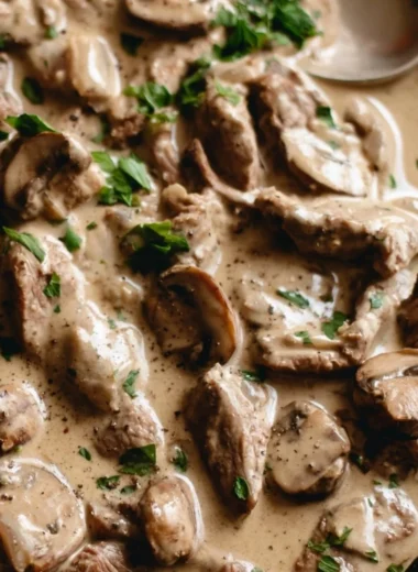 A hearty bowl of beef stroganoff served with egg noodles and garnished with parsley.